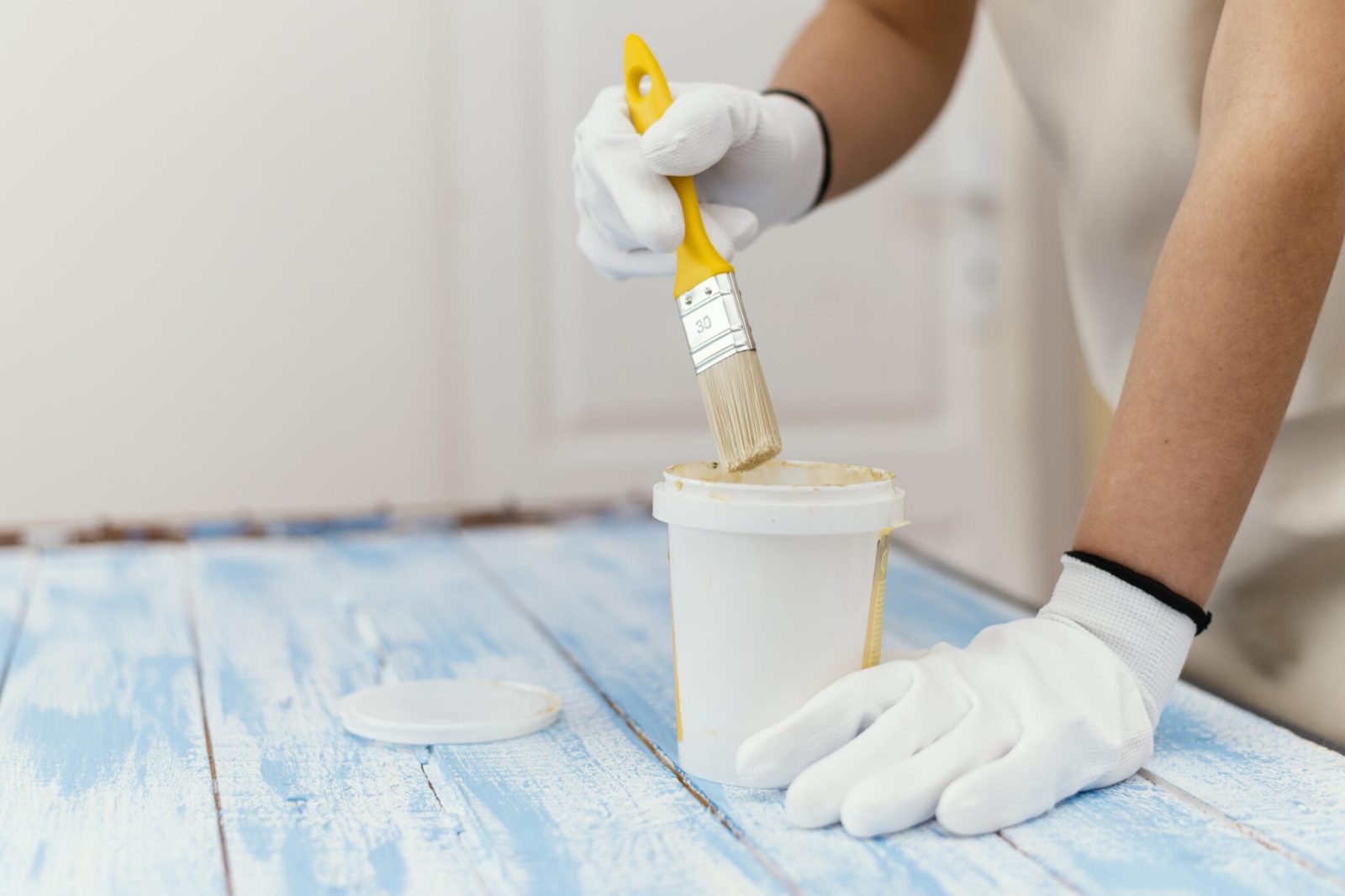A close up of a painter using a brush to seal a paint distressed blue wooden panel